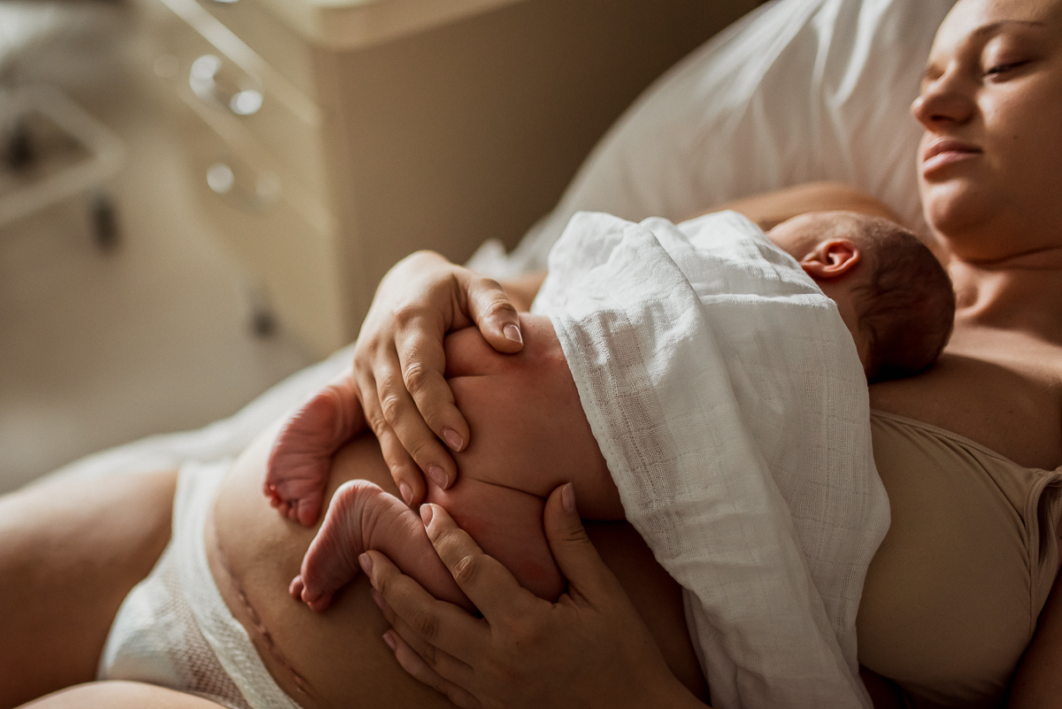 mama z raną po cesarskim cięciu trzyma nowonarodzone dziecko