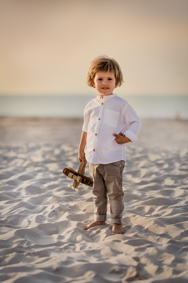 chłopiec bawi się drewnianym samolotem na plaży