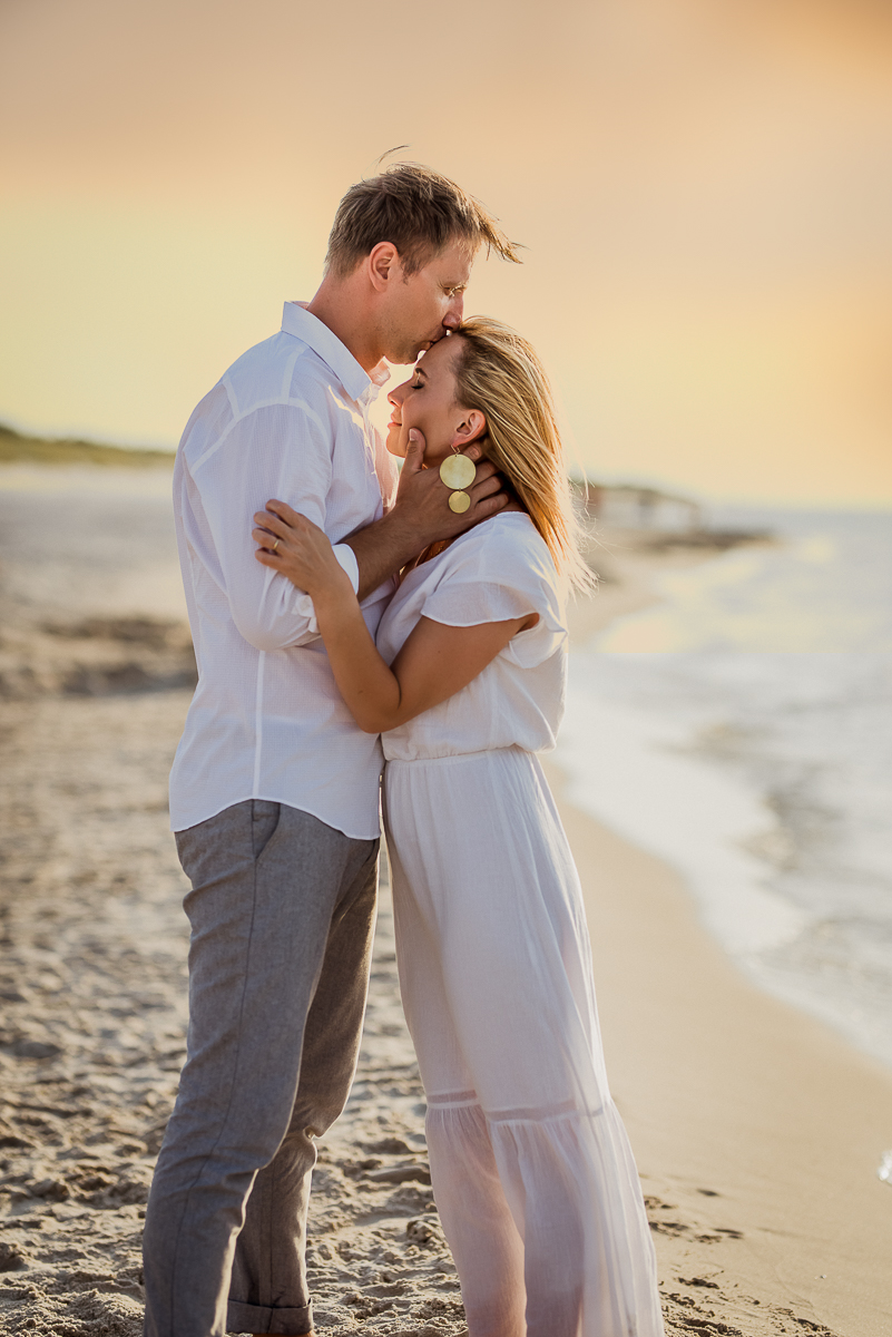 mężczyzna całuje w czoło swoją żonę na plaży