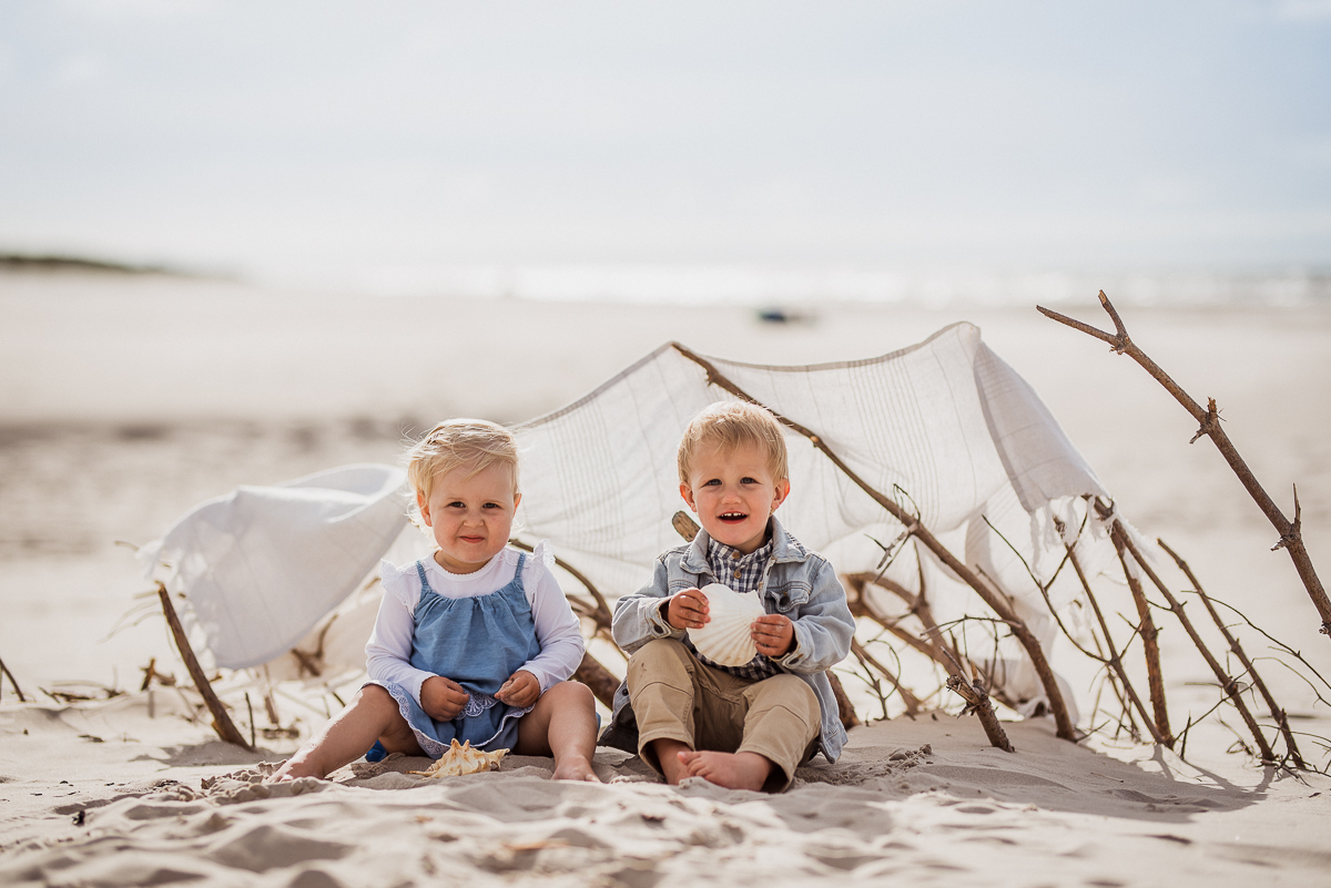 2 latki razem na plaży nad Bałtykiem siedzą pod namiotem w otoczeniu patyków