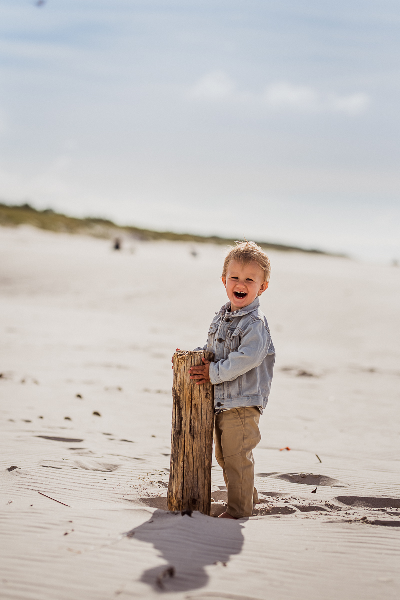 chłopiec uśmiecha się na plaży trzyma drewniany pal
