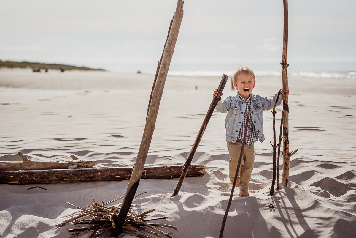 chłopiec uśmiecha się na plaży trzyma drewniane kija badyle