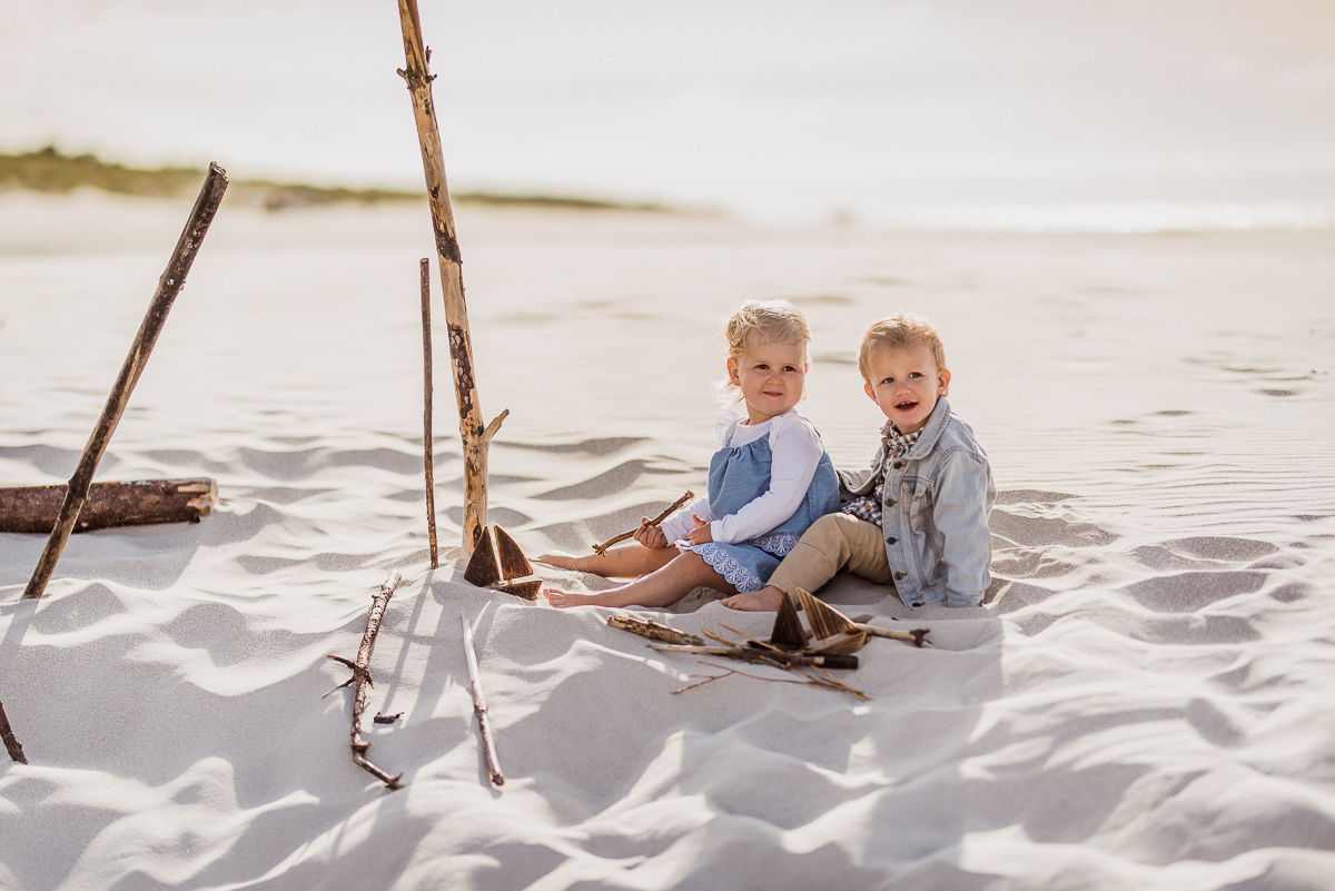dzieci 2 letnie przytulają się na plaży siedząc na piasku 